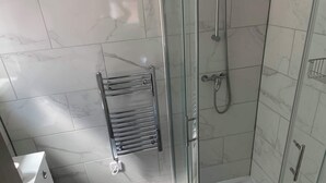 Moderni kylpyhuone, jossa on lasinen suihkuseinä, lasiovi ja marmorilaatoitettu seinä.