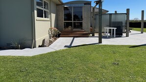 Ein Haus mit überdachter Veranda, einem kleinen Tisch im Freien und einem Rasen.