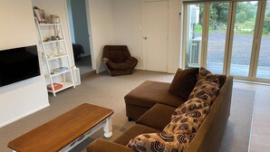 Ein Wohnzimmer mit braunem Sofa, einem Holztisch, einer weißen TV-Konsole und einem Bücherregal.