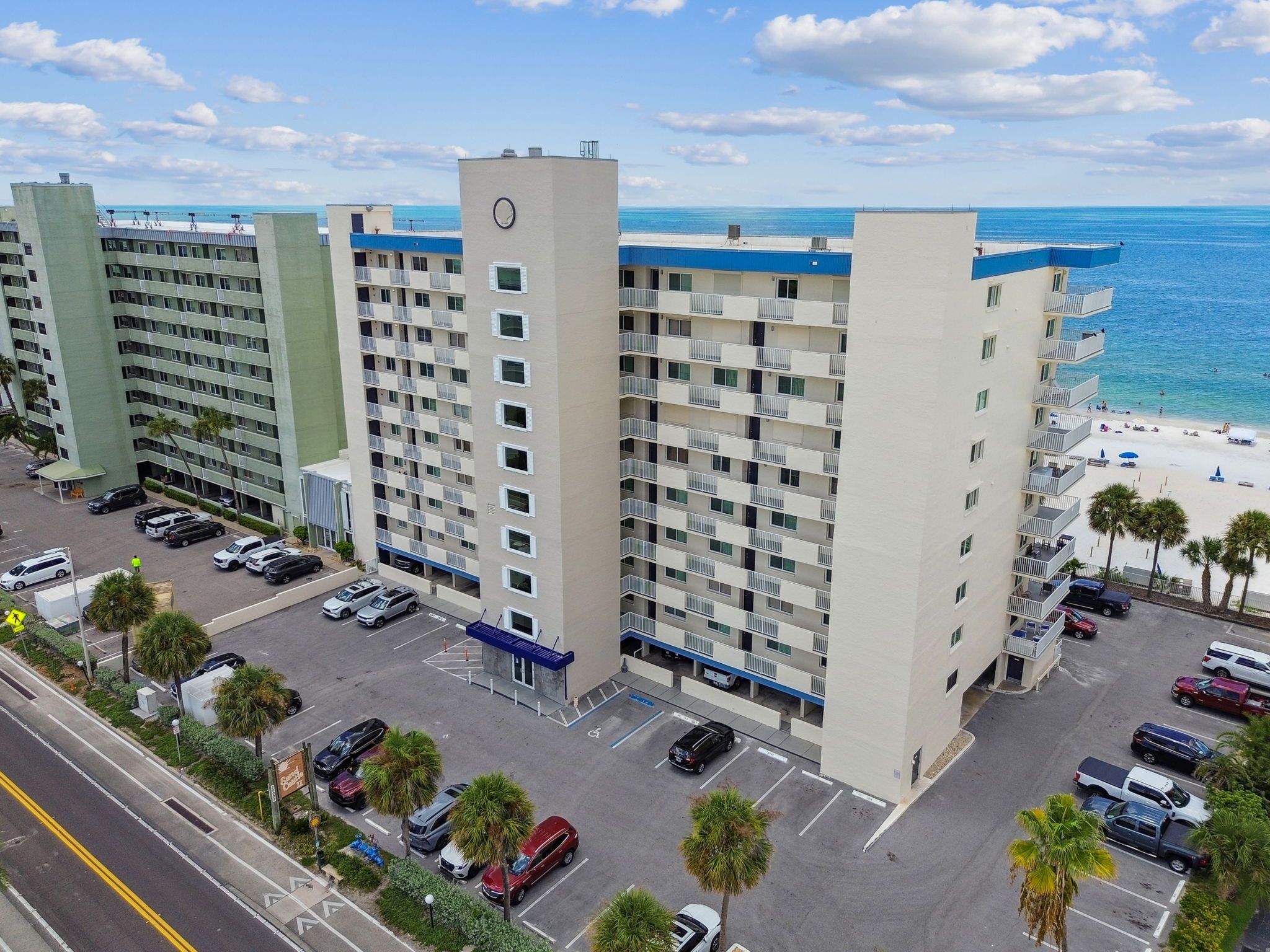 Un hôtel à plusieurs étages dot é d’un parking, offrant une vue sur la plage et comprenant un beffroi.