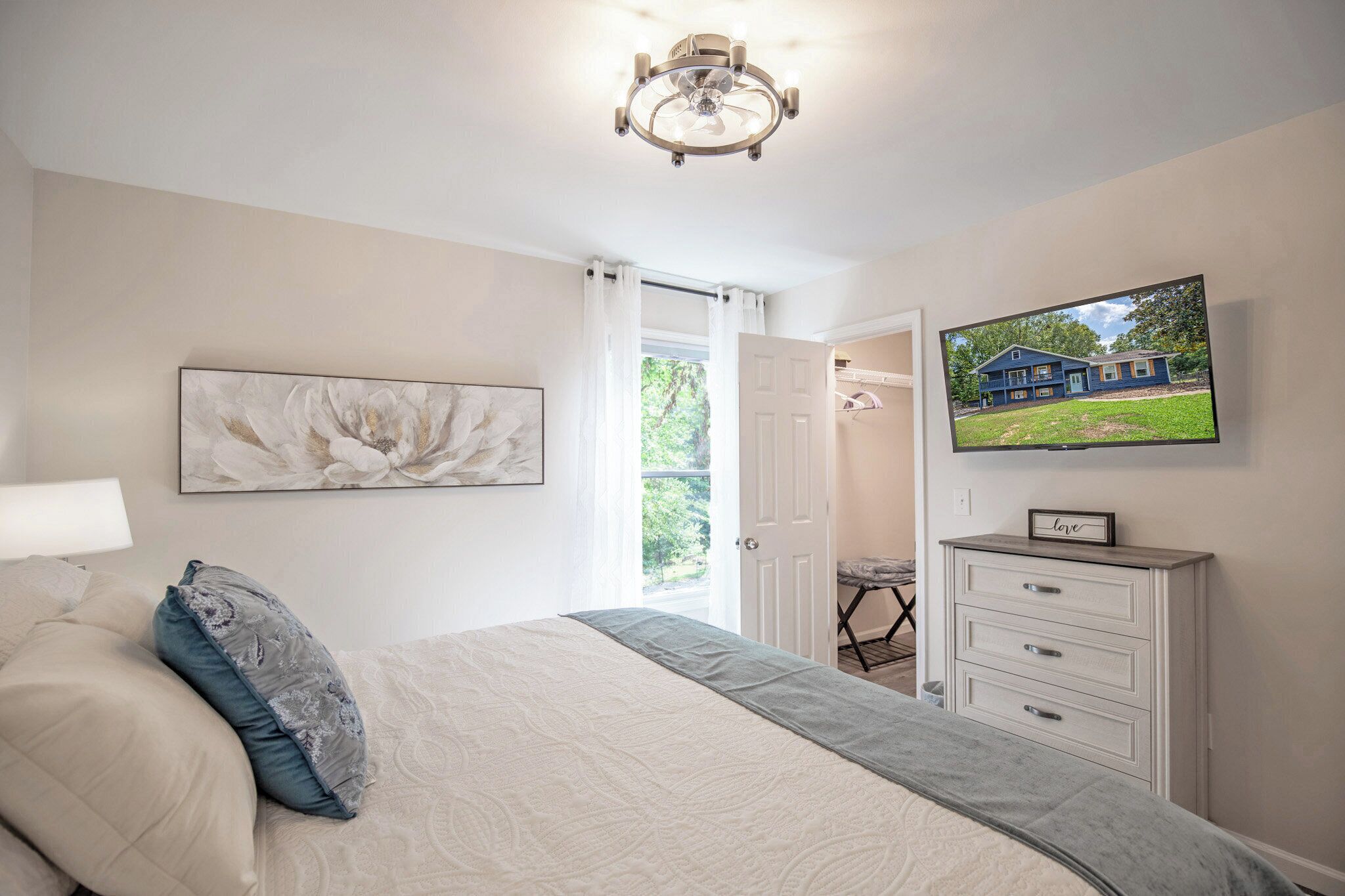 Un dormitorio con una cama, televisor, cómoda y una puerta que da a un balcón.