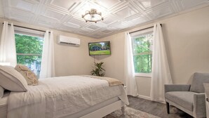 Un dormitorio con cama, una silla, un televisor y un ventilador de techo.
