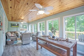 Eine Veranda mit Korbmöbeln, einem Holztisch und einem Deckenventilator.
