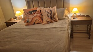A neatly made bed with a beige blanket and decorative pillows, two bedside tables with lamps, and a wooden nightstand with a remote control.