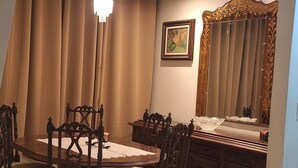 A dining area with a round table, chairs, a chandelier, curtains, a cabinet, and a mirror.