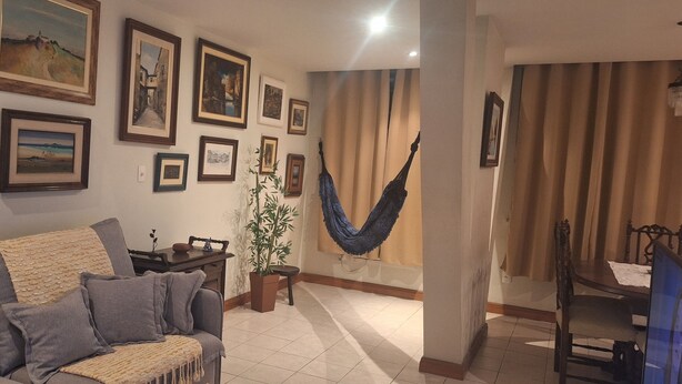 A living room with a sofa, a hammock, and various framed artworks on the wall.