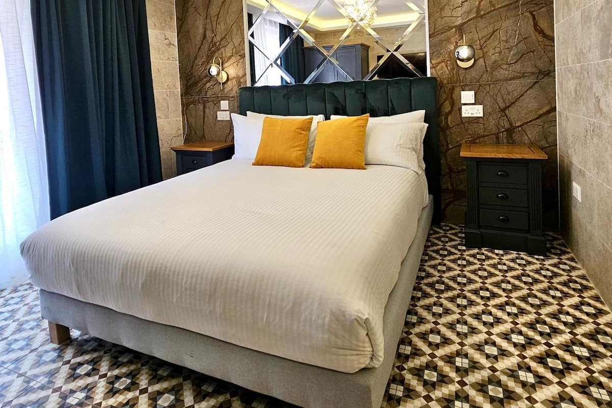A hotel room with a large bed, a chandelier, a clock, and a patterned floor.