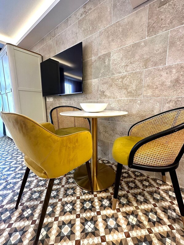 Un comedor moderno con una mesa redonda, dos sillas amarillas, un tazón blanco, un televisor de pantalla plana montado en una pared de piedra y un piso con estampado.