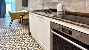 A modern kitchen with white cabinets, a built-in oven, and a microwave. There is a dining area with a table and chairs. - Balcony Hotel (St. Julian's)