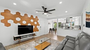 Una sala moderna con un televisor de pantalla plana, sofá de cuero, decoración hexagonal de madera y un ventilador de techo.