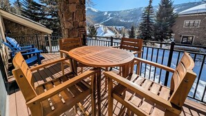 Une terrasse en bois avec une table ronde et des chaises, offrant une vue sur un paysage montagneux enneigé.