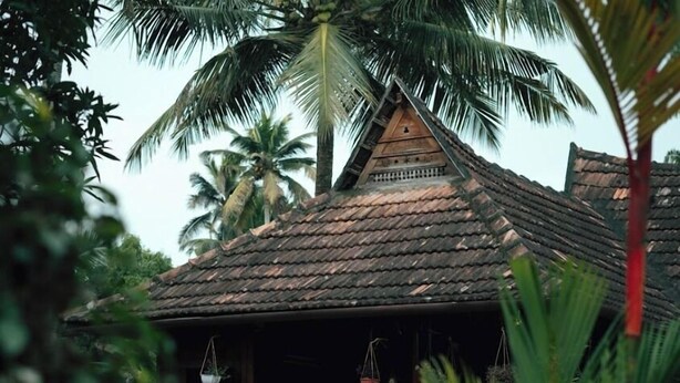 A traditional house with a tiled roof, surrounded by lush greenery and palm trees. - Tentgram Alleppey Riverfront  (Vaikom)