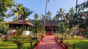 A traditional building with a tiled roof, surrounded by lush greenery and palm trees. - Tentgram Alleppey Riverfront  (Vaikom)