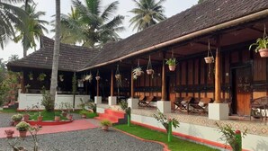 A traditional building with a thatched roof, outdoor seating area with chairs, and potted plants. - Tentgram Alleppey Riverfront  (Vaikom)