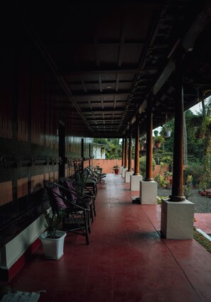 A covered outdoor area with rows of chairs and tables, potted plants, and a red tiled floor. - Tentgram Alleppey Riverfront  (Vaikom)