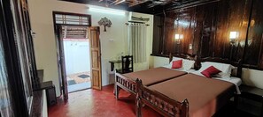 A room with a wooden bed, a small table, and a door leading outside. - Tentgram Alleppey Riverfront  (Vaikom)