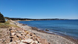 Un littoral rocheux bordé d’une mer d’un bleu limpide, une petite maison et, au loin, une zone boisée.