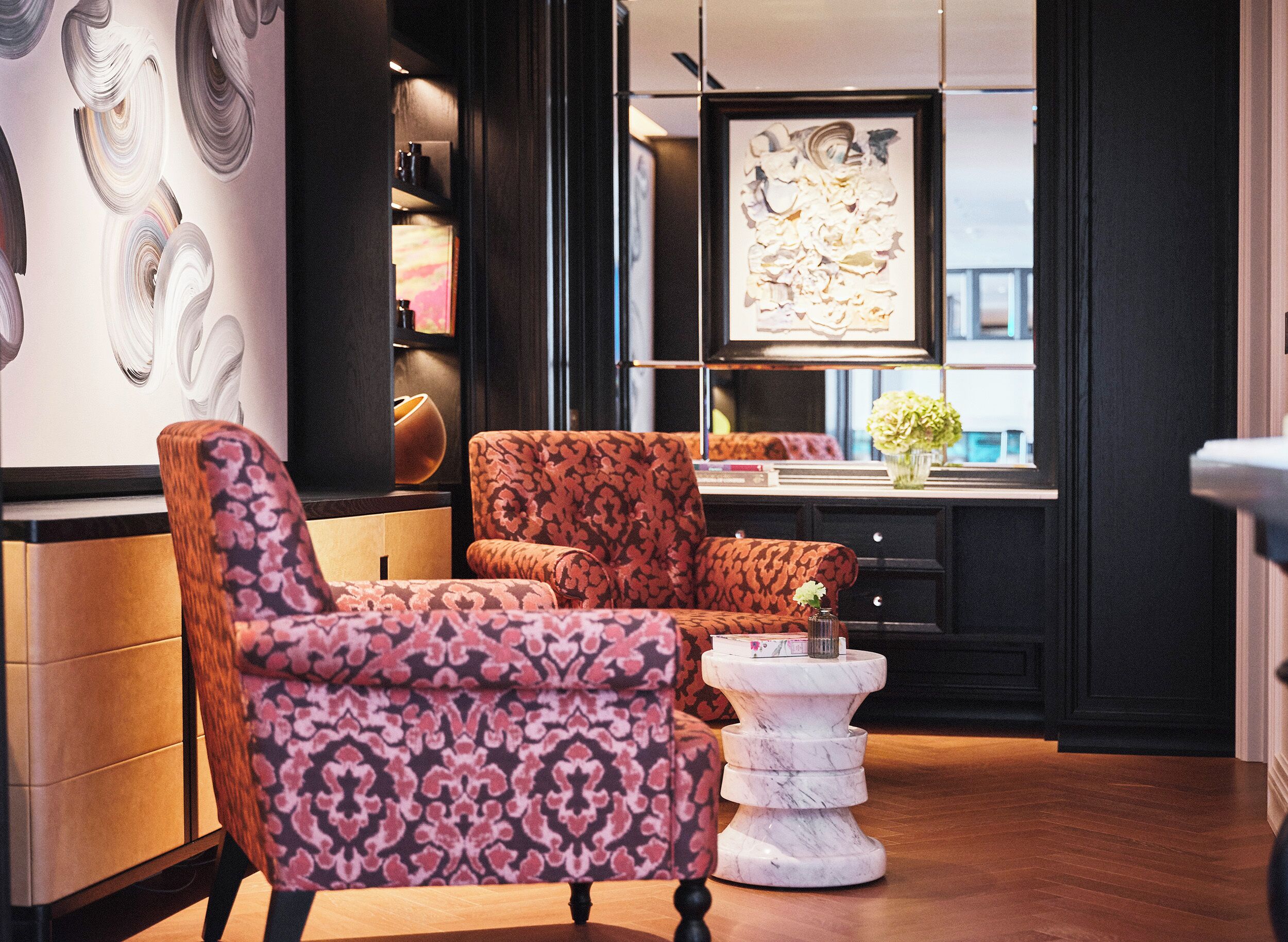 A modern living room with a patterned armchair, a white side table, and a large abstract painting on the wall.