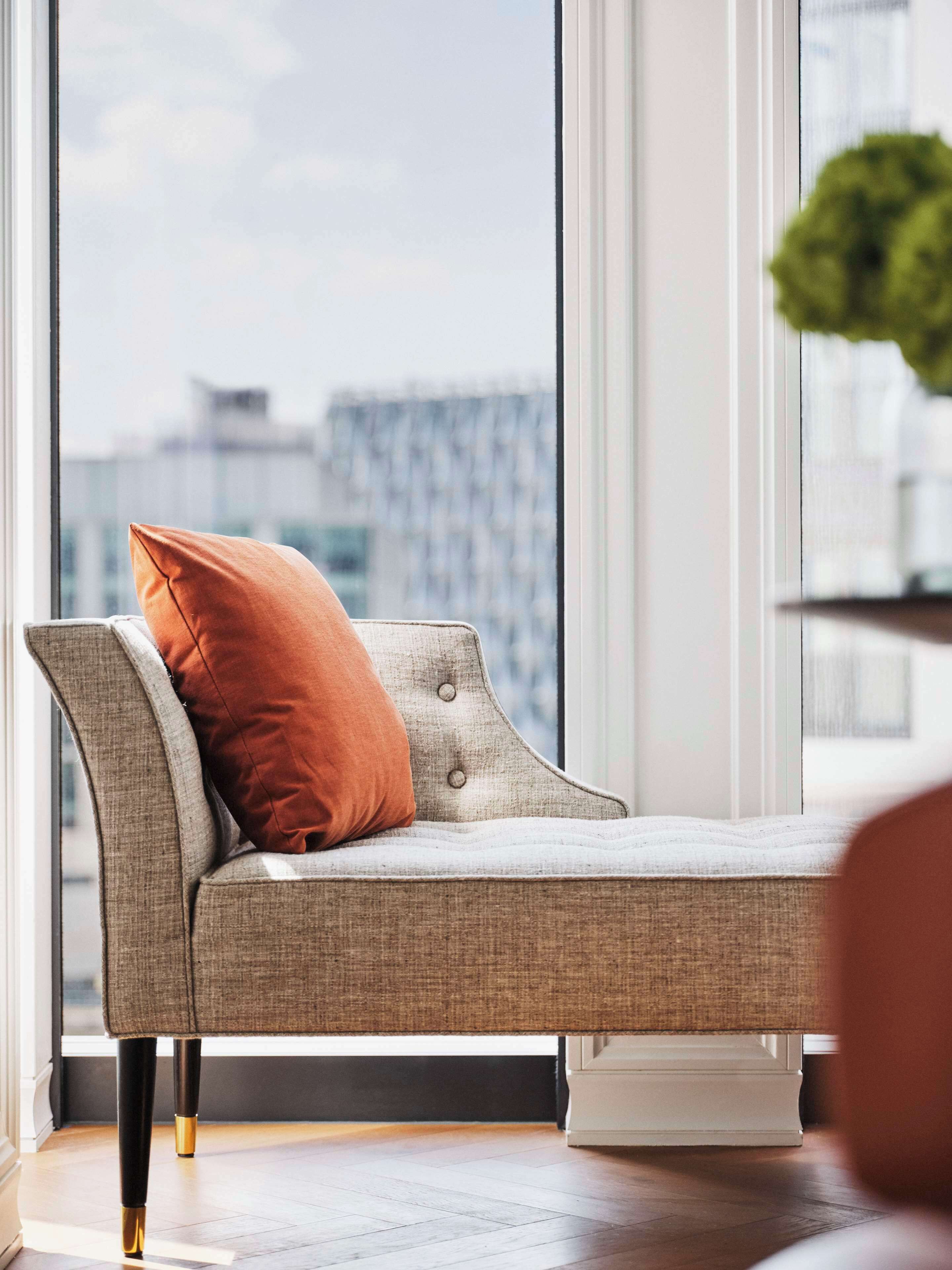 A modern sofa with a cushion, positioned in front of a large window with a view of a cityscape.