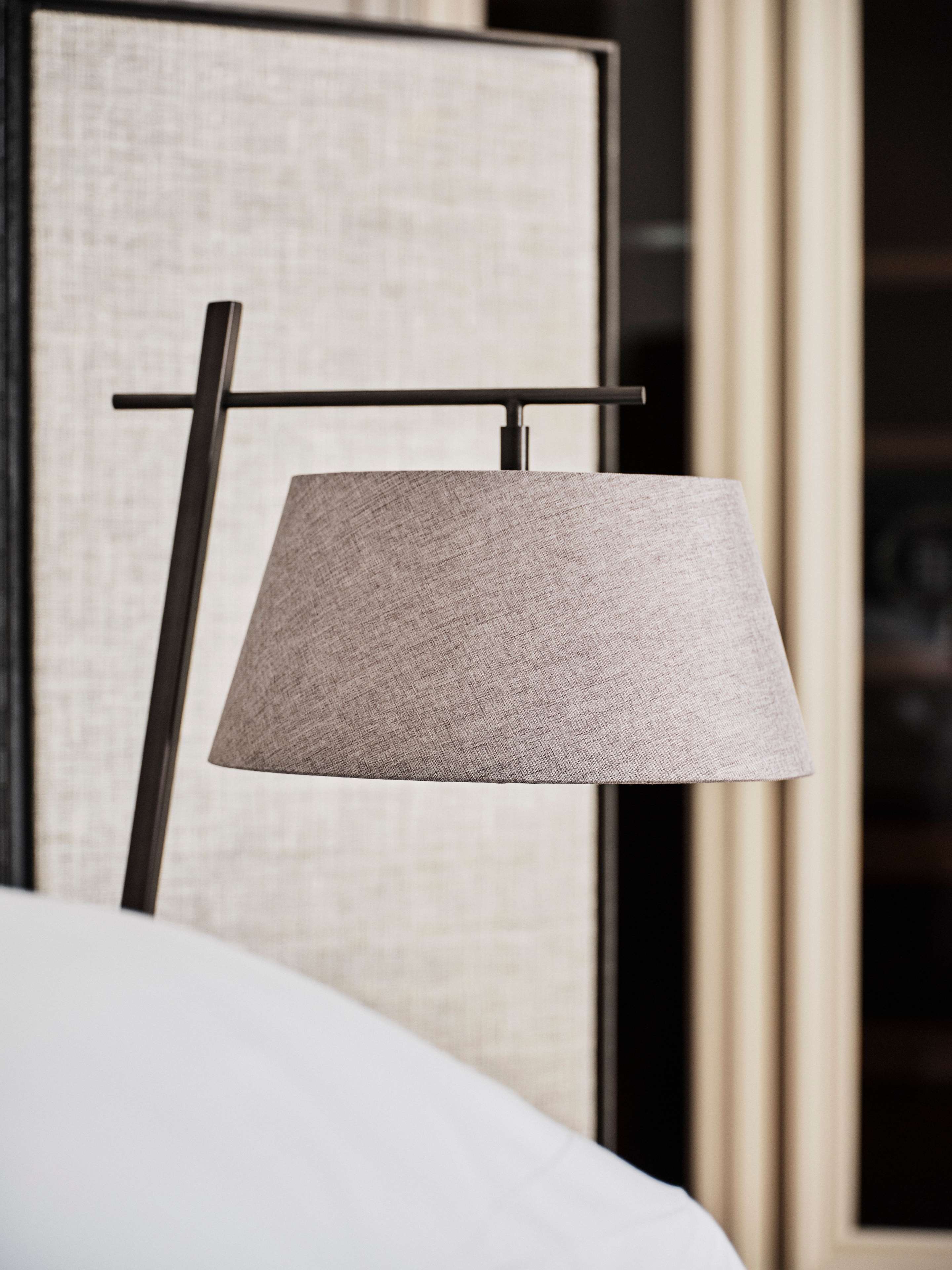 A modern lamp with a textured shade, mounted on a black metal stand, in a room with a large framed artwork on the wall.