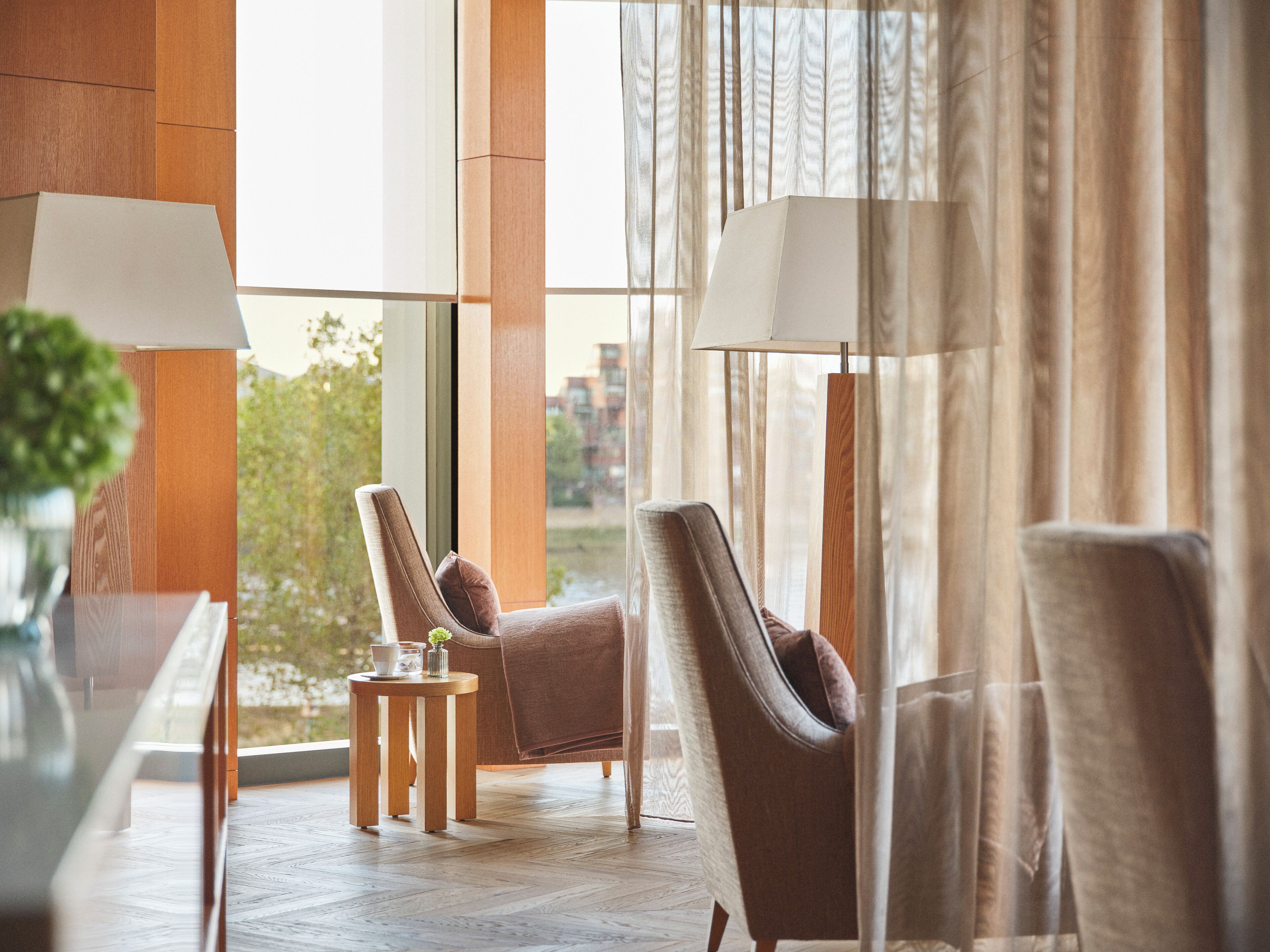 Habitació d'hotel moderna amb una finestra gran, dos seients còmodes, una taula auxiliar petita i una làmpada.