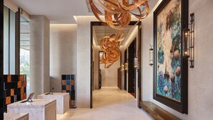 Een moderne hotellobby met marmeren receptiebalies, een grote abstracte sculptuur en een kleurrijk schilderij aan de muur.