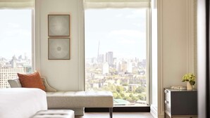 Ein modernes Schlafzimmer mit Stadtblick, einem Bett, einer Bank und einem kleinen Nachttisch mit einer Vase.