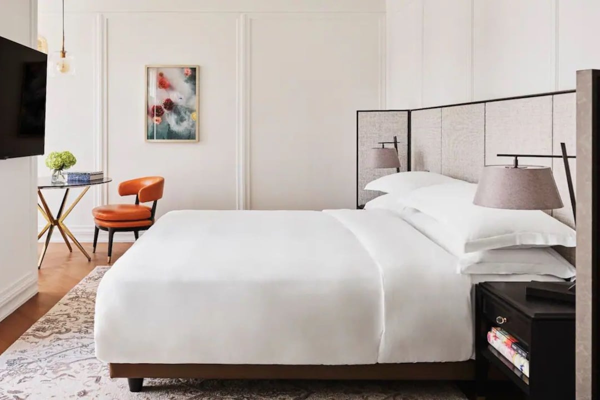 Une chambre d’hôtel moderne, dotée d’un grand lit, d’une télévision, d’un bureau avec une chaise et d’un tableau au mur.