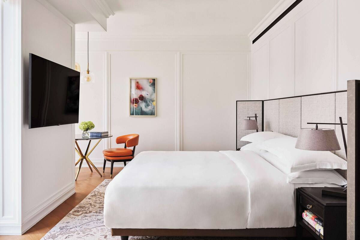 Ein modernes Schlafzimmer mit einem großen Bett, einem Schreibtisch mit Stuhl, einem Fernseher und Bildern an der Wand.