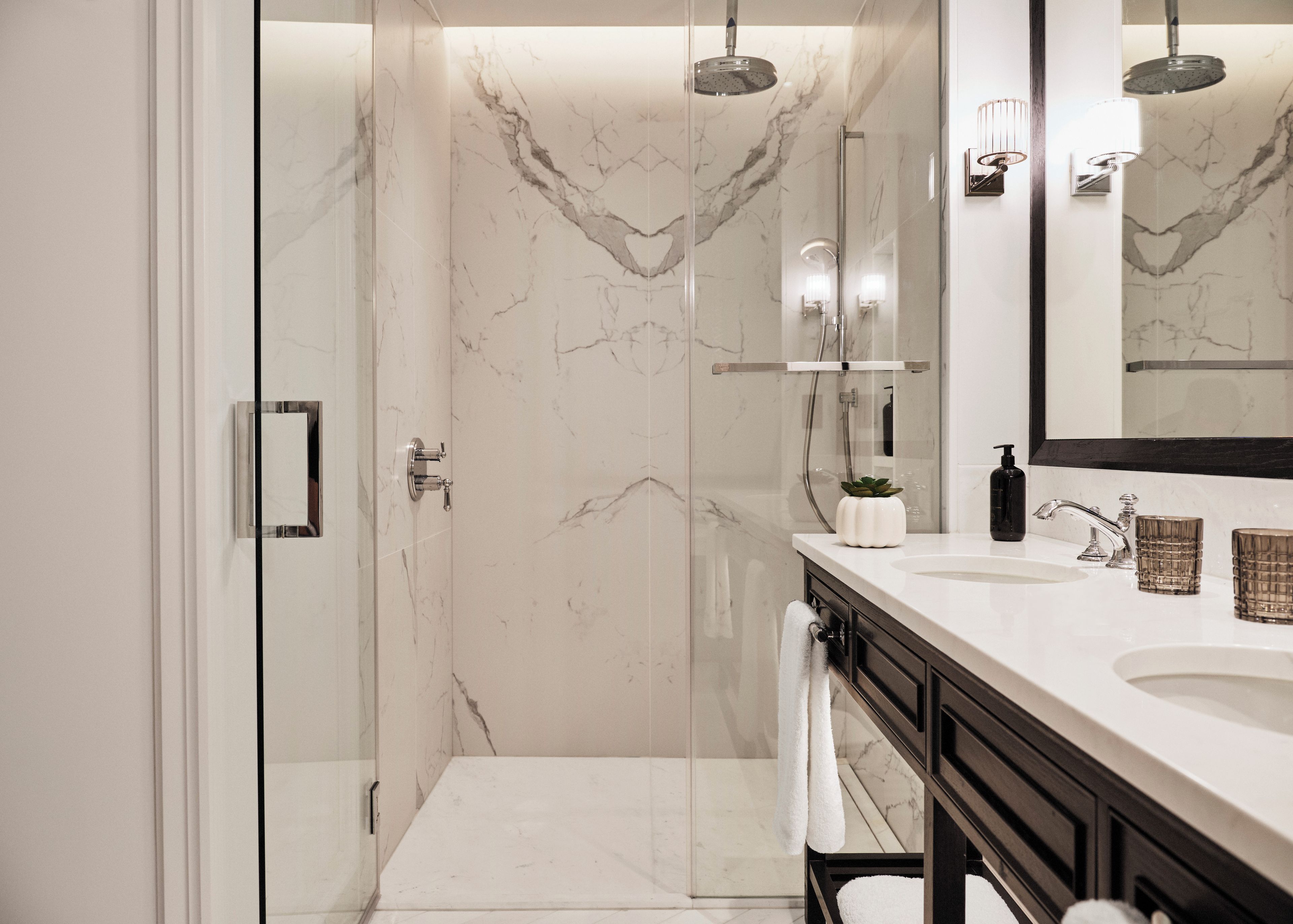 A modern bathroom with a glass-enclosed shower, a white marble wall, and a vanity with a large mirror.