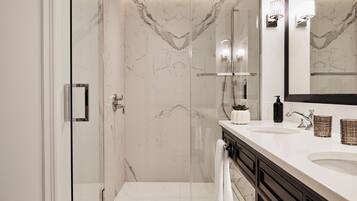 Une salle de bain moderne avec une douche à parois de verre, un mur en marbre blanc et un meuble-lavabo doté d’un grand miroir.