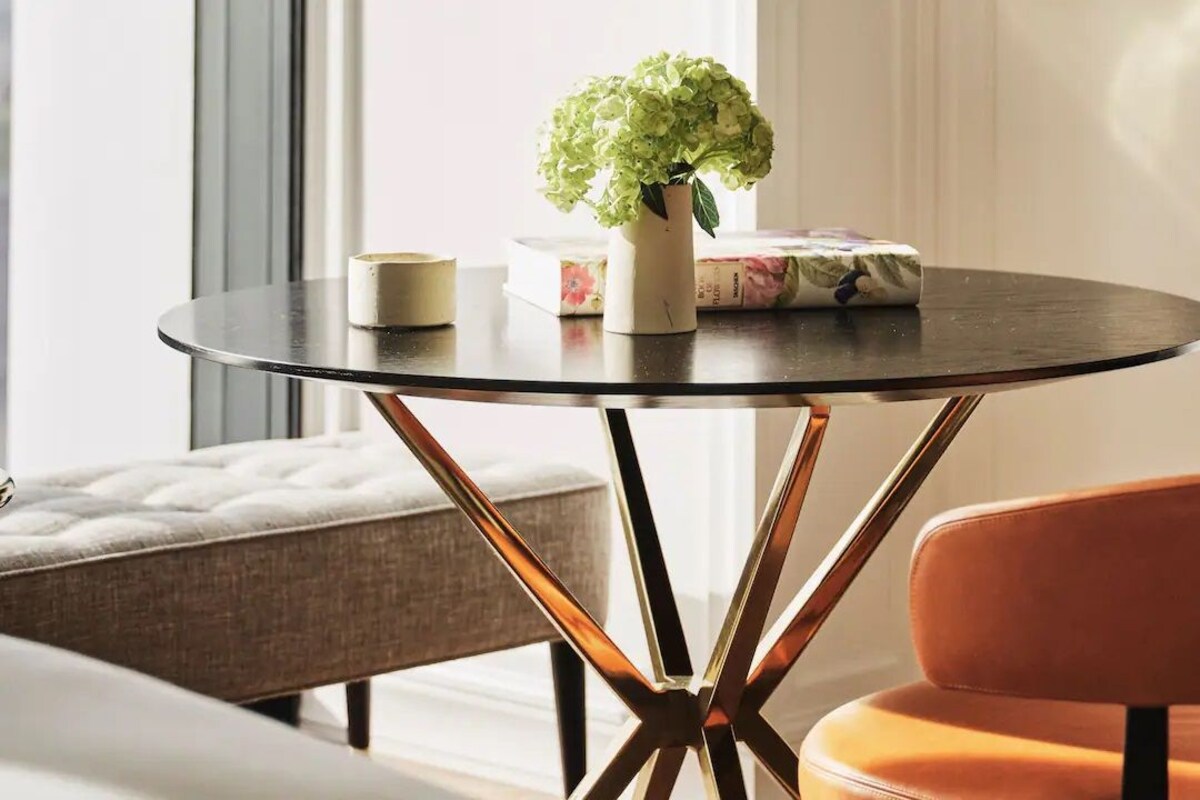 Une table ronde ornée d’un vase de fleurs et de quelques livres, un banc rembourré et une chaise moderne.