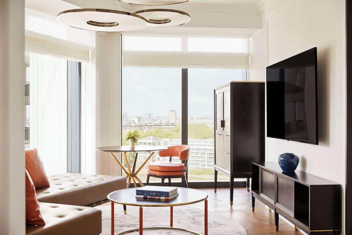 Ein modernes Wohnzimmer mit einer Couch, einem runden Couchtisch, einem an der Wand befestigten Fernseher und Blick auf die Stadt durch große Fenster.