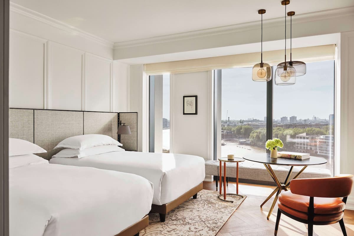 Ein modernes Hotelzimmer mit zwei Betten, einem runden Tisch mit einer Vase und Blick auf die Stadt durch große Fenster.