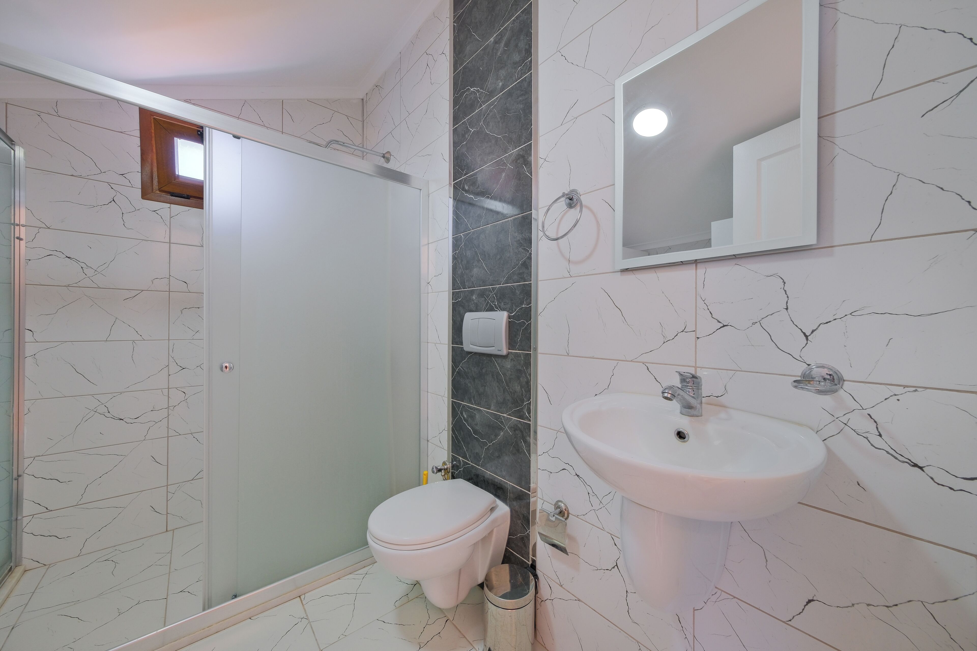 A bathroom with a glass-enclosed shower, a toilet, and a sink with a mirror above it.