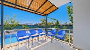 Ein überdachter Balkon mit blauen Plastikstühlen und einem Pool im Hintergrund.