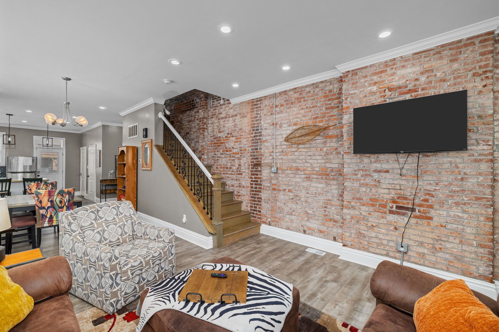 Un salon avec un mur en briques, un téléviseur à écran plat fixé au-dessus, un escalier et, au fond, un coin repas.