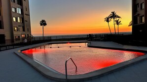 En swimmingpool med udsigt til solnedgang, omgivet af bygninger og palmer.