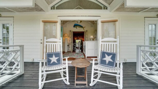 A porch with two rocking chairs and a table, leading to a hallway with a ceiling fan and a lamp. - Family vacation on AMI w/pool 4BR, 2.5BA, up to 8 guests (Holmes Beach)