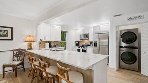 A modern kitchen with white cabinetry, a central island with bar stools, a built-in microwave, and a stainless steel refrigerator. - Family vacation on AMI w/pool 4BR, 2.5BA, up to 8 guests (Holmes Beach)