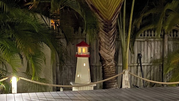 A wooden deck with a rope barrier, a small white lighthouse, and a palm tree. - Americana AMI Lighthouse 3BR w/pool + rooftop deck (Holmes Beach)