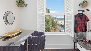 Une pièce avec une fenêtre, une chaise, une table, une plante suspendue et un portant à vêtements.