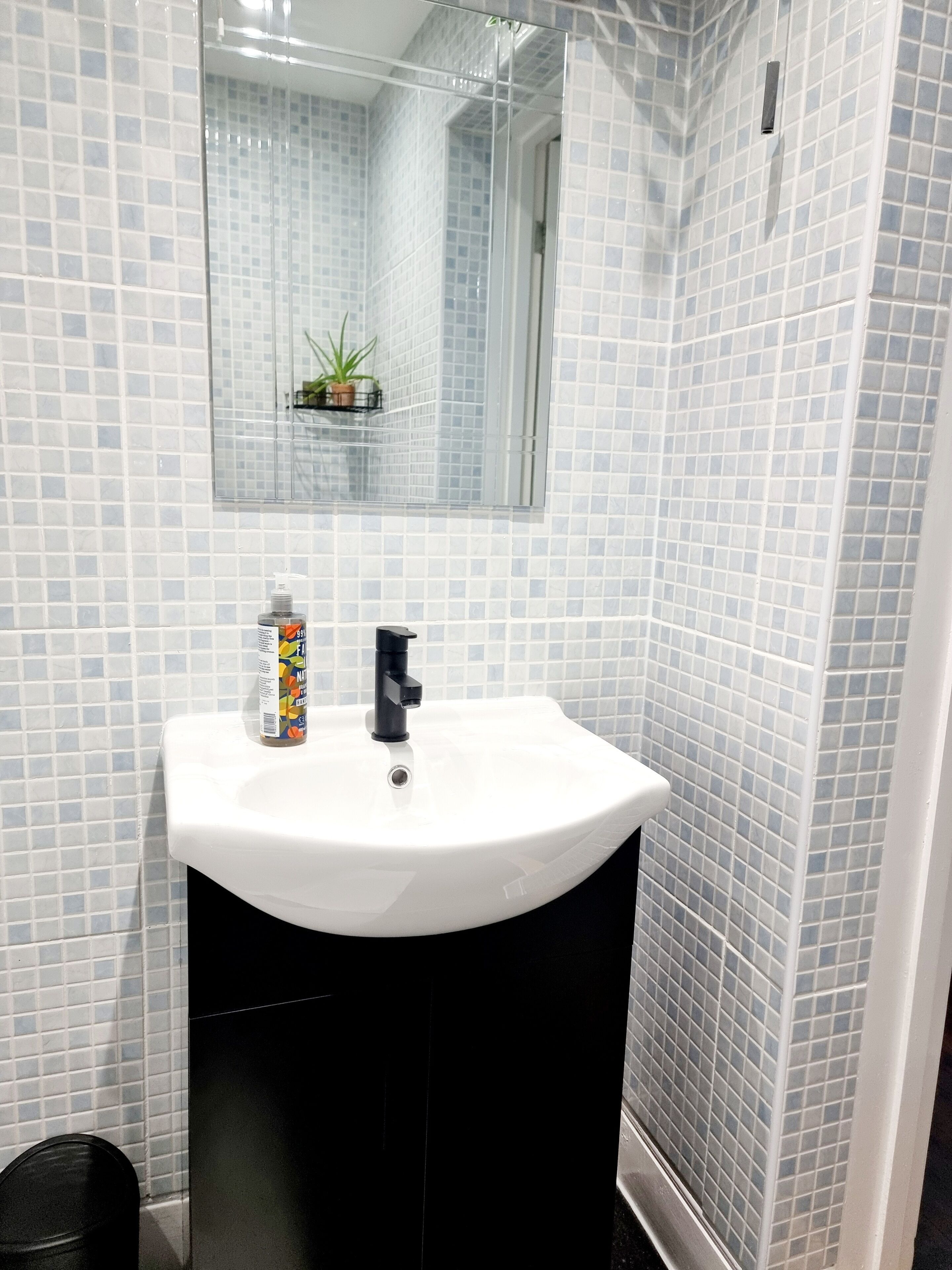A bathroom with a white sink, black cabinet, and tiled walls.