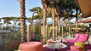 A terrace with round tables and chairs, a glass balustrade, and a view of trees and mountains. -  Magic Forte (Forte dei Marmi)