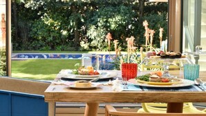 An outdoor dining area with a table set for two, surrounded by greenery and a pool view. -  Magic Forte (Forte dei Marmi)