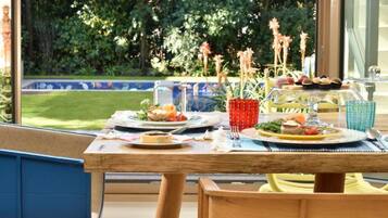 Un espace de restauration en plein air avec une table dressée pour deux personnes, entouré de verdure et offrant une vue sur la piscine.