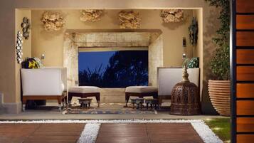 Un espace extérieur accueillant, aménagé avec un foyer, deux fauteuils confortables, une petite table et des éléments décoratifs.