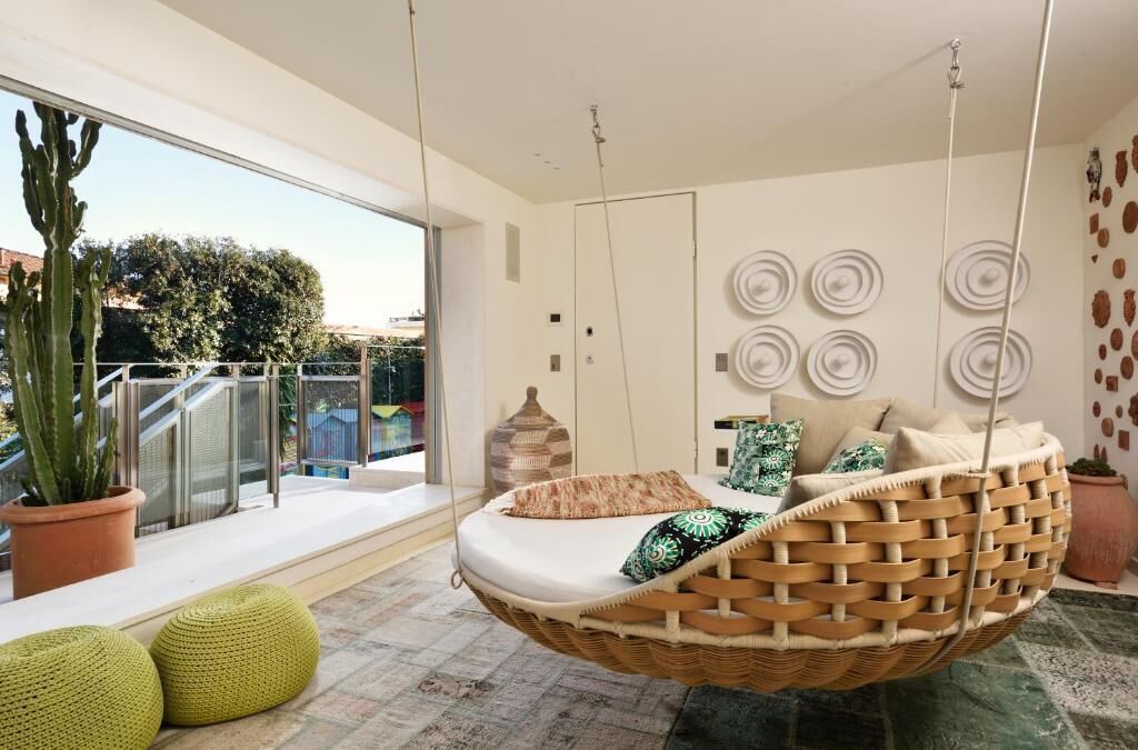 Une chambre moderne avec un fauteuil suspendu, une grande fenêtre et un cactus.