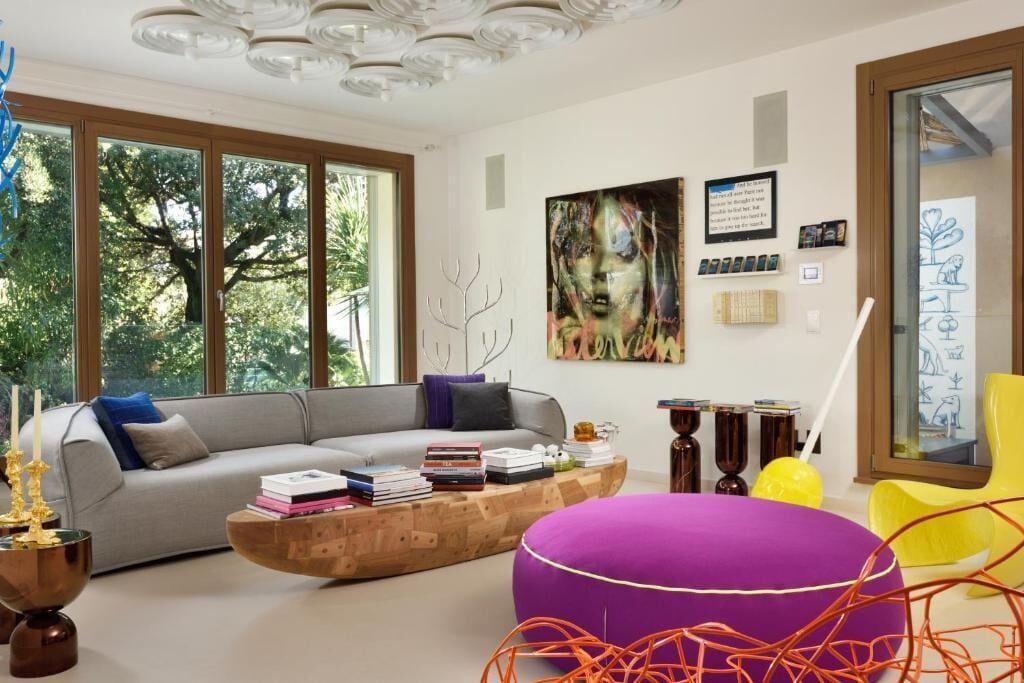 Un soggiorno moderno con un divano grigio, un tavolino in legno e un poggiapiedi viola vivace.