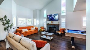 A spacious living room with a fireplace, a pool table, and a television displaying a movie.